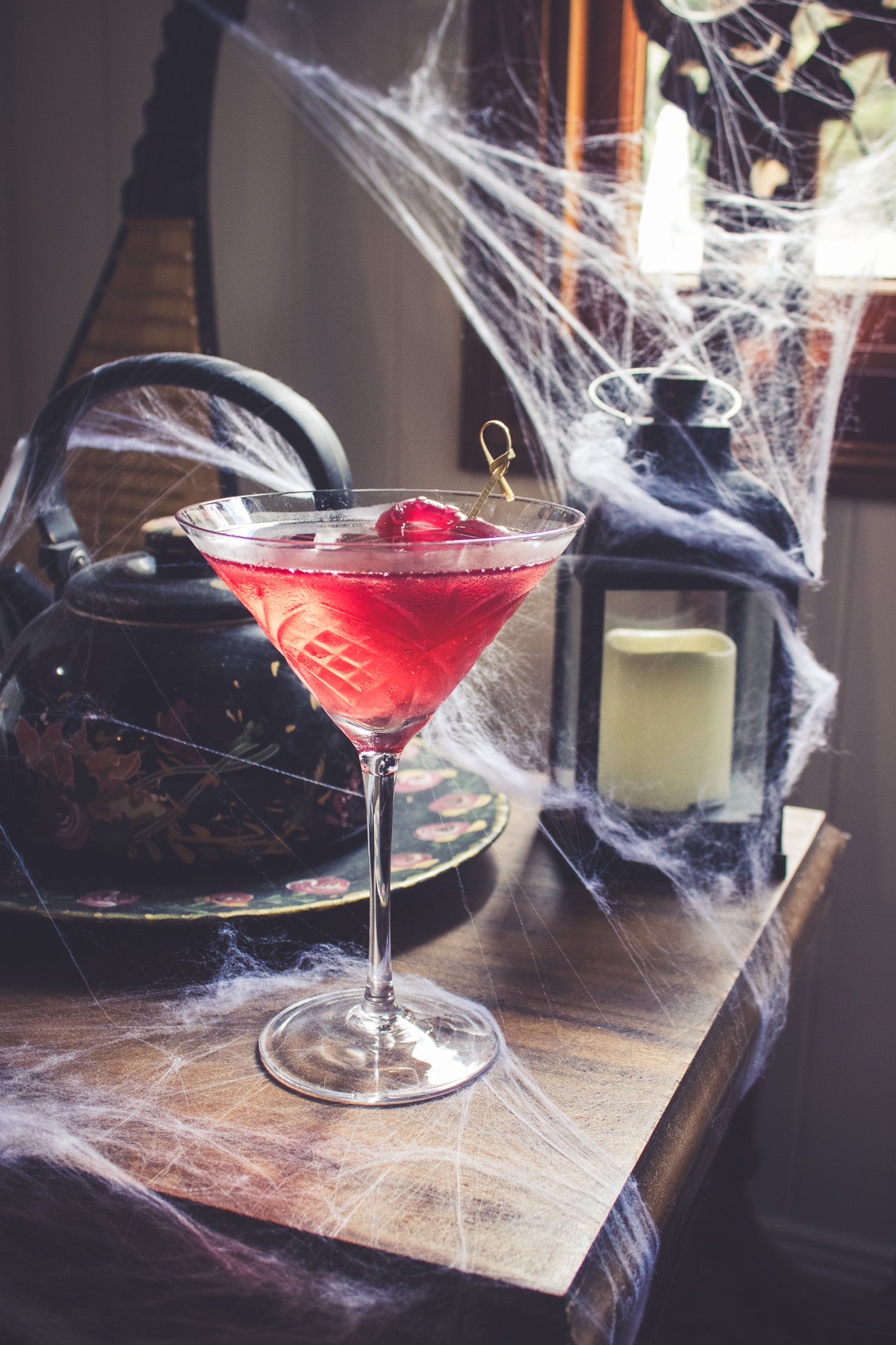 Red cocktail with a cherry on a wooden table with spider webs and lanterns.