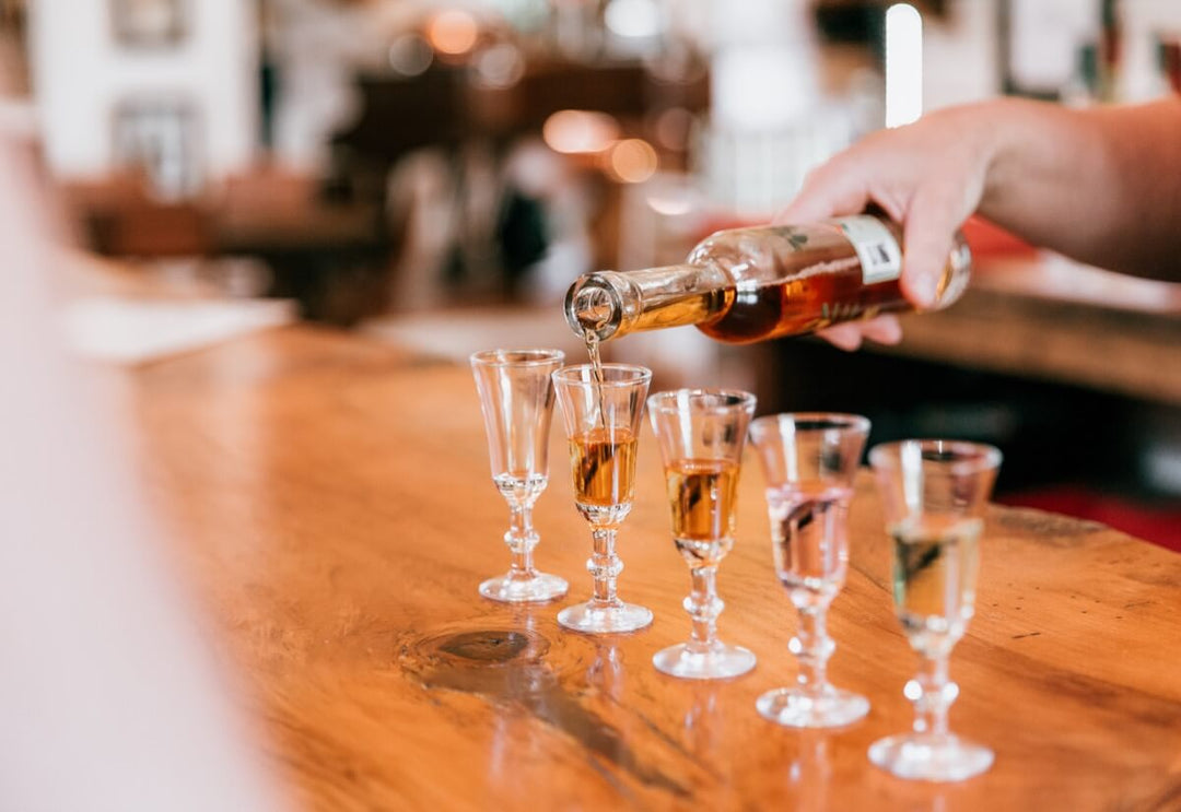 row of five glasses lined up and being filled with liquor