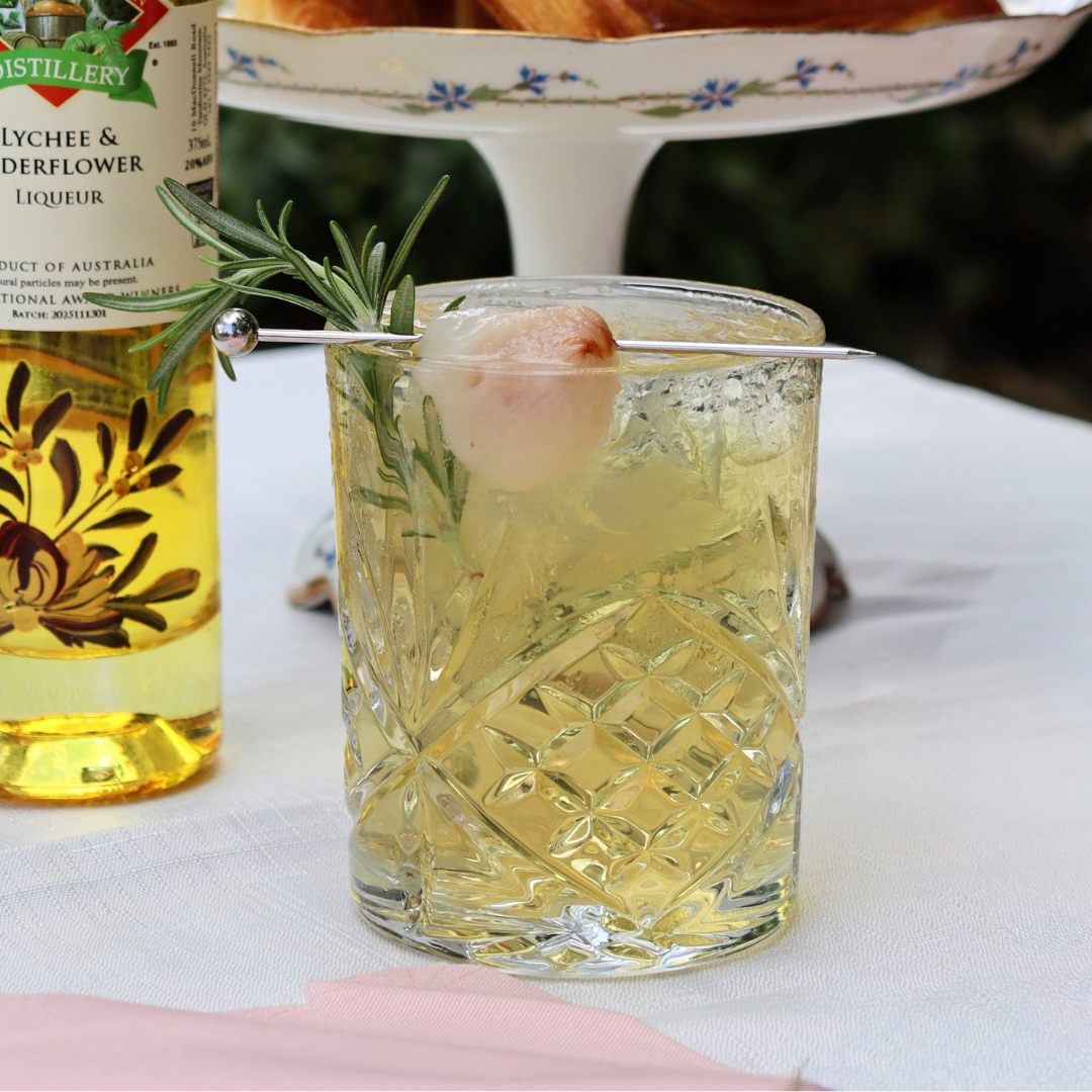 Whisky glass with ice, yuzu gin, lychee and elderflower liqueur, topped with tonic, garnished with rosemary and lychee skewer.