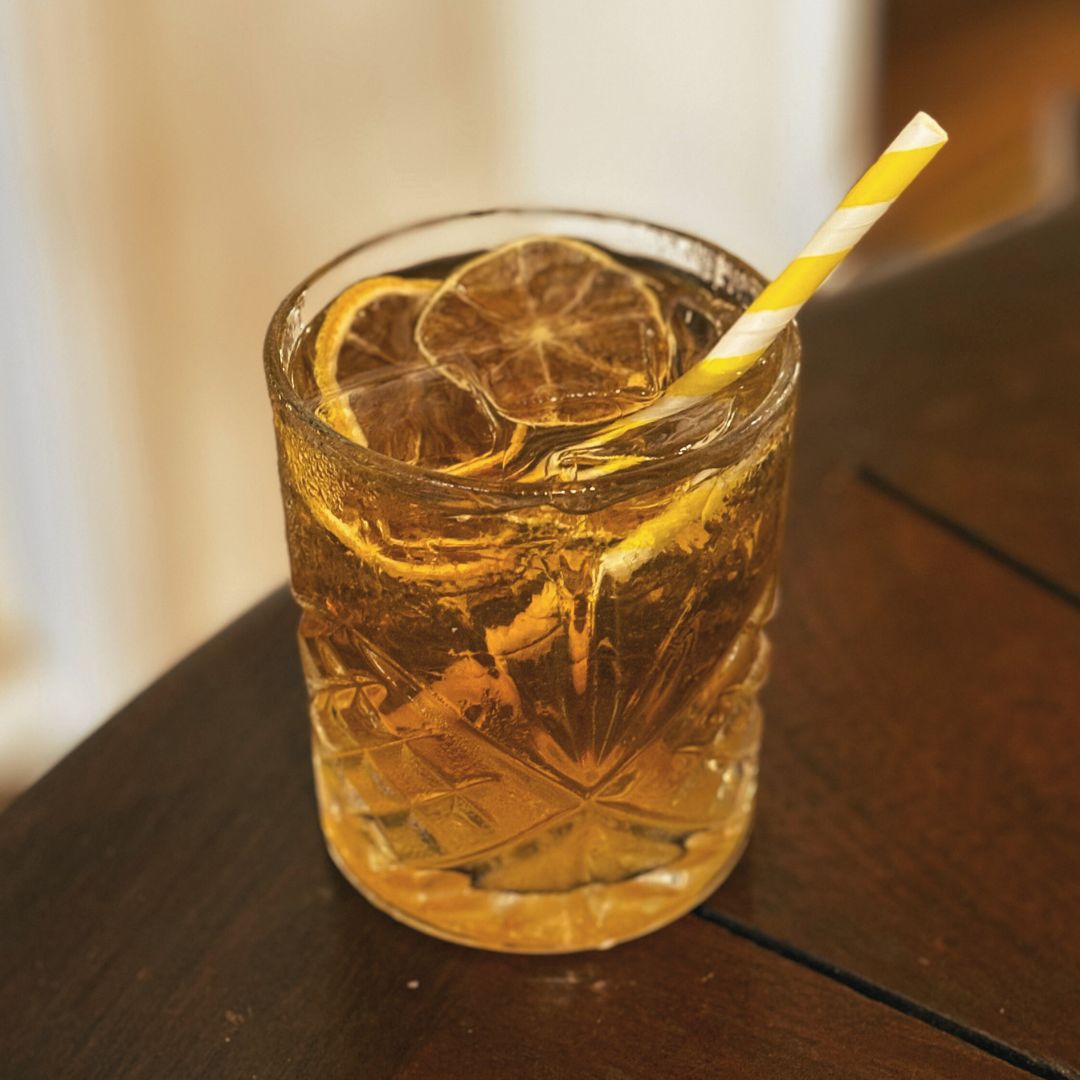Golden Storm cocktail with Spiced Gold Rum, Lime Liqueur, and dry ginger ale, served over ice in a whiskey glass with dried lime slices.
