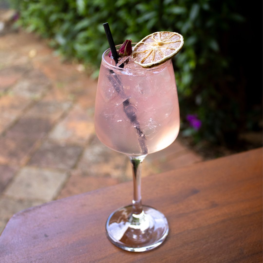 Spring Bloom cocktail in a wine glass with a lemon twist and edible flower, made with TMD Lilly Pilly Gin, Hibiscus Liqueur, lemon juice, simple syrup, and sparkling wine.