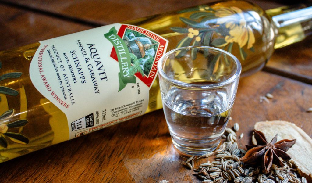 Aquavit bottle and poured shot glass styled with fennel seeds and caraway spices on a rustic surface
