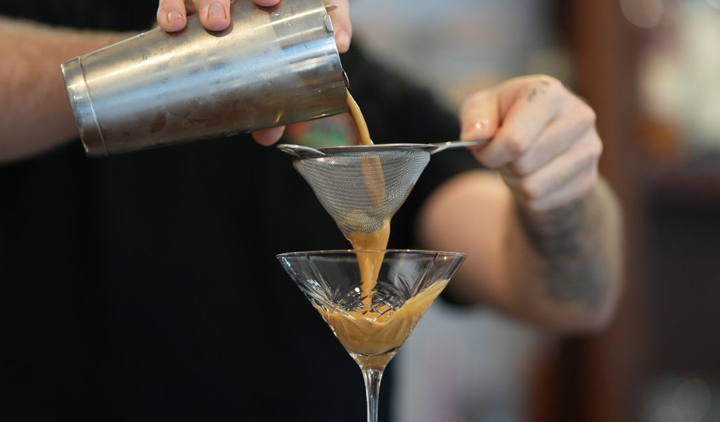 Bartender carefully pouring an Espresso Martini to create a smooth, velvety finish.