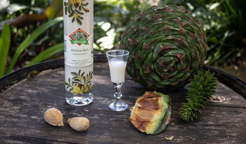 Bottle of Bunya Nut Cream Liqueur displayed beside shelled bunya nuts on a wooden surface.
