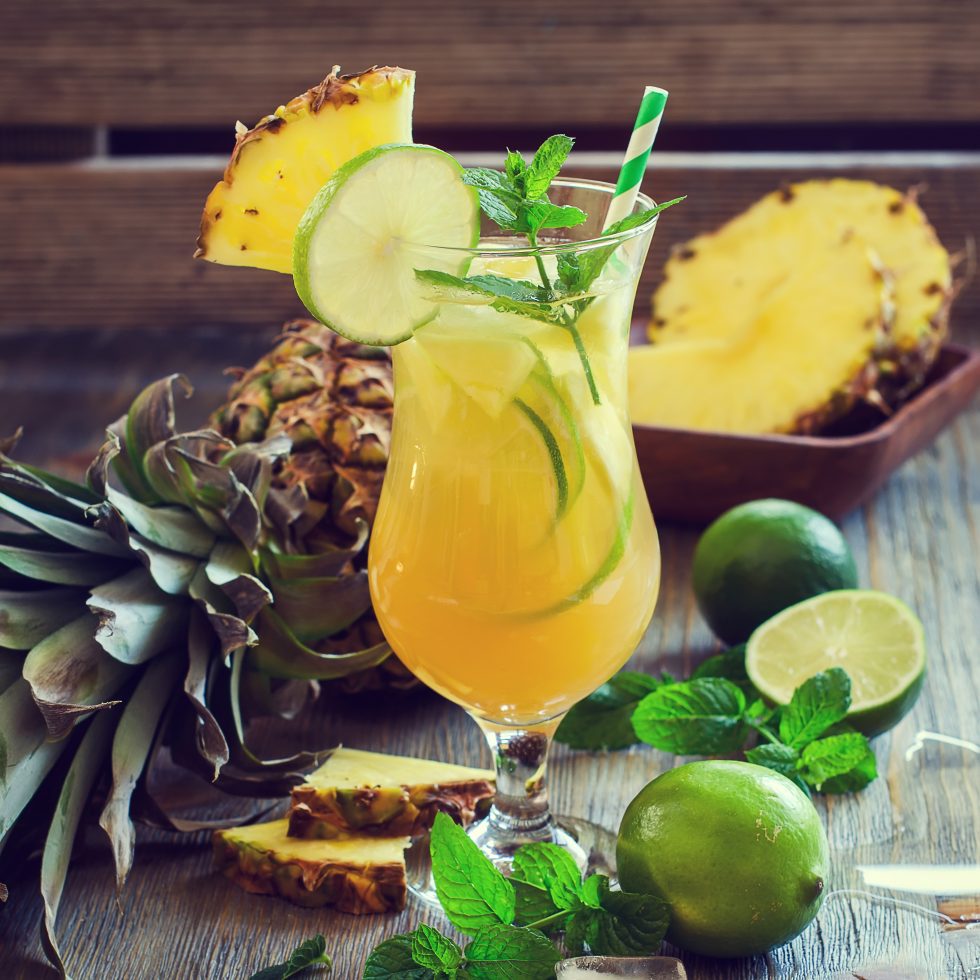 Tropical Breeze cocktail with Gold Rum, Banana and Passionfruit Liqueurs, pineapple and orange juices, served over ice in a Tulip glass with pineapple and lime garnish.