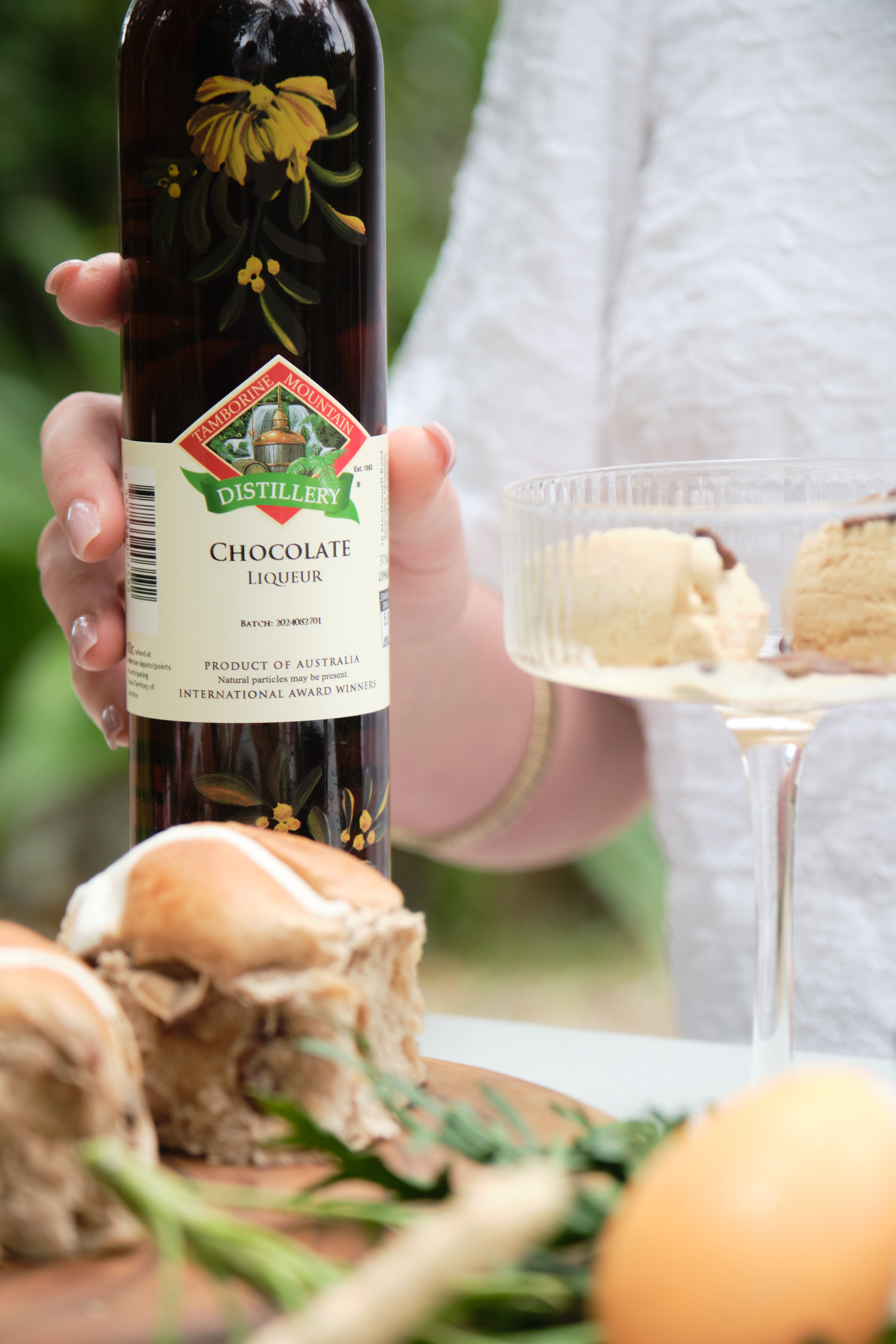 Bottle of Tamborine Mountain Distiller's Chocolate Liqueur held by a person with ice cream and cookies on a table.
