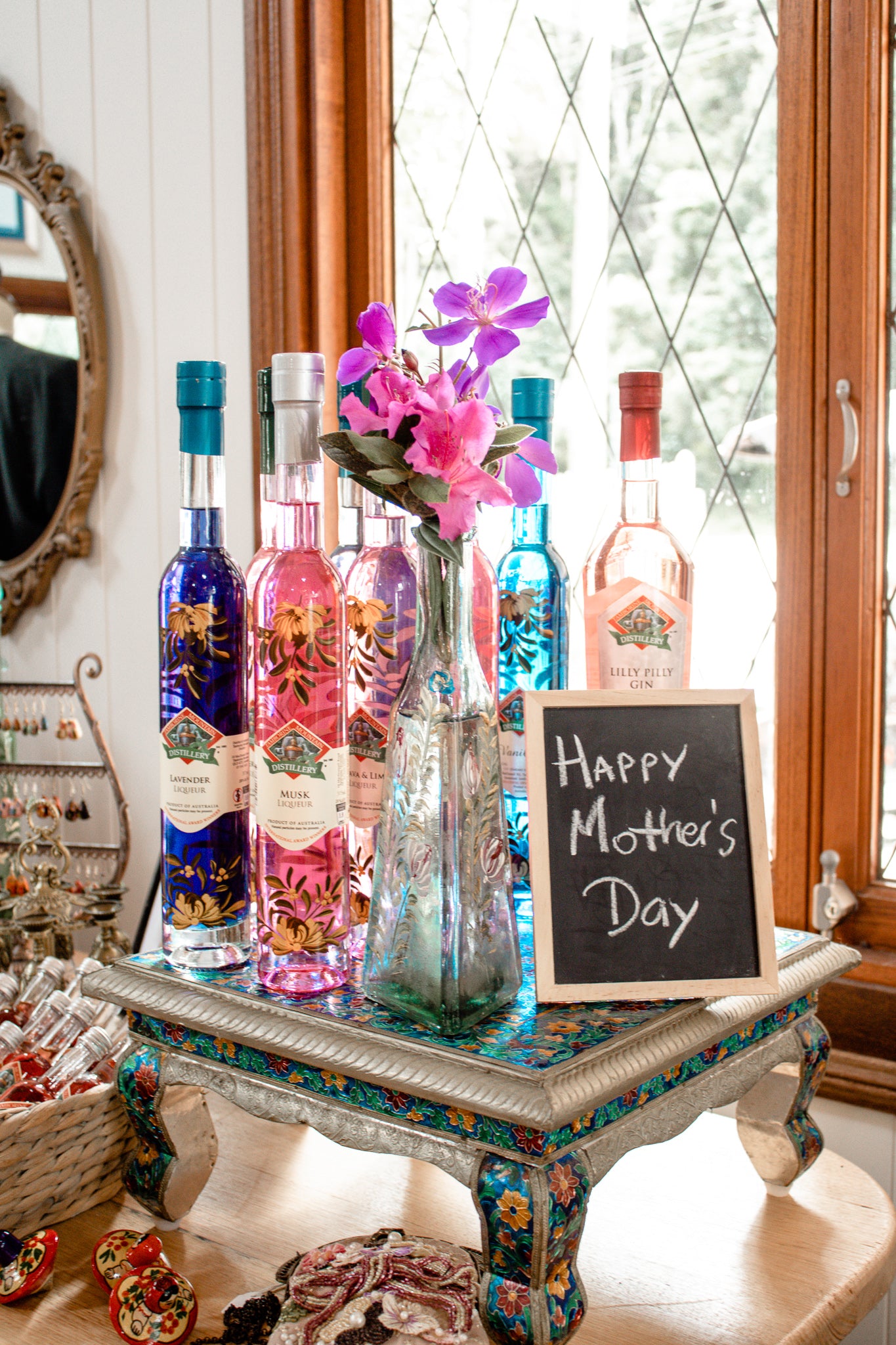 Decorative table with colorful bottles, flowers, and a 'Happy Mother's Day' sign.