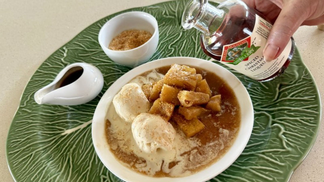 Bowl of ice cream with apple pieces on a green plate, accompanied by a bottle of spiced Christmas Liqueur.