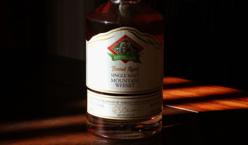 Bottle of single malt mountain whiskey from Tamborine Mountain Distillery on a wooden surface with a dark background