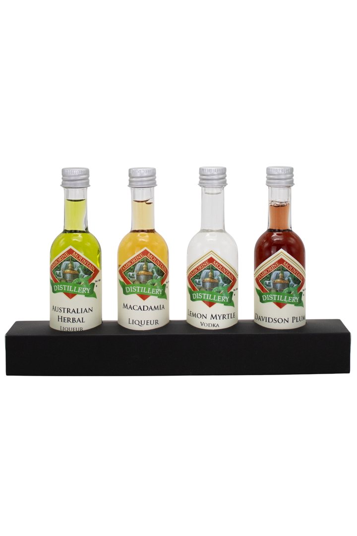 Four miniature liquor bottles displayed on a black rectangular stand against a plain white background. The bottles include Australian Herbal, Macadamia Infused, Rum Myrtle, and Whiskey Punch, each with a silver cap and a green and red label.